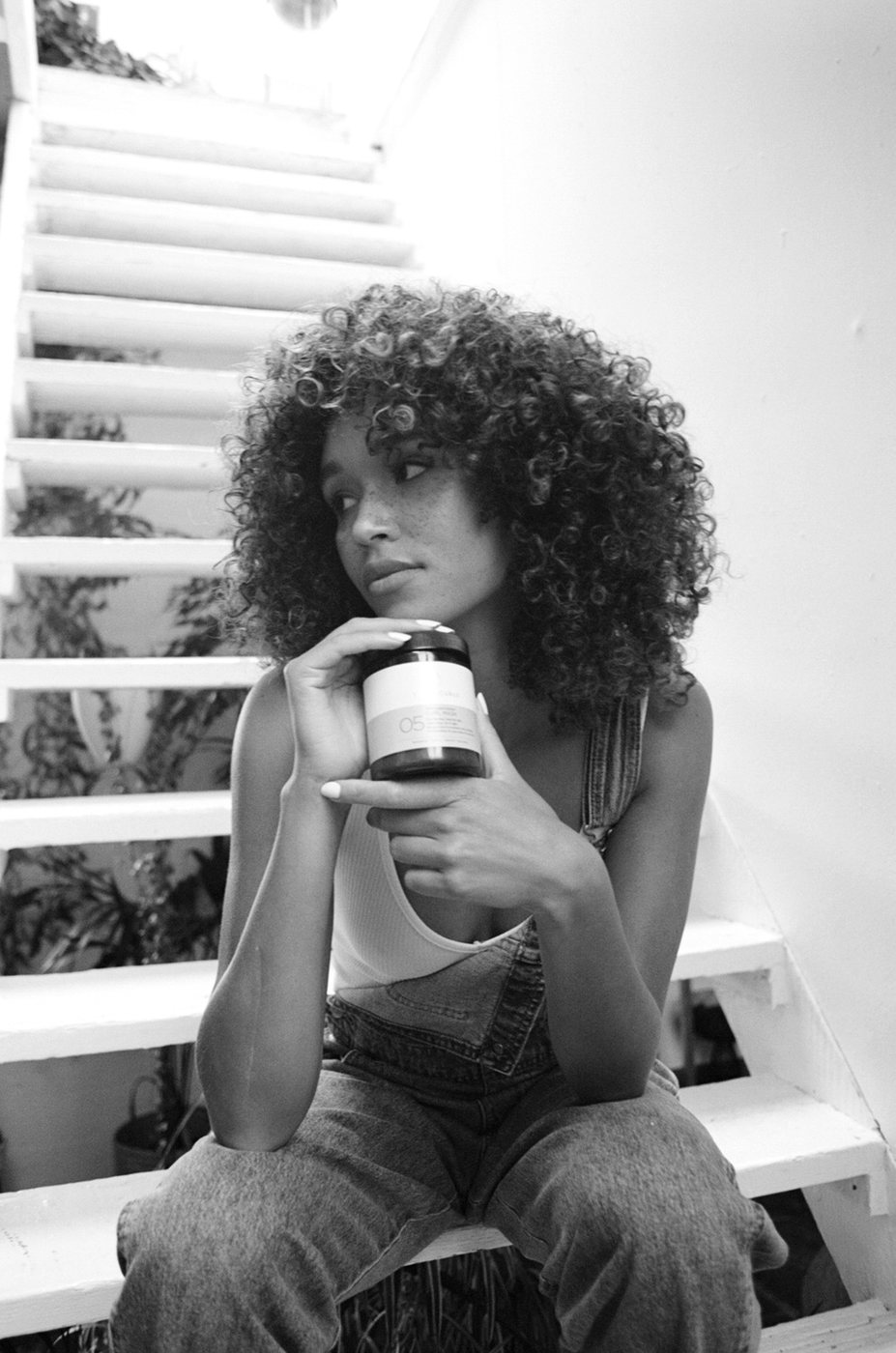 A woman with curly hair holding a scalp care product